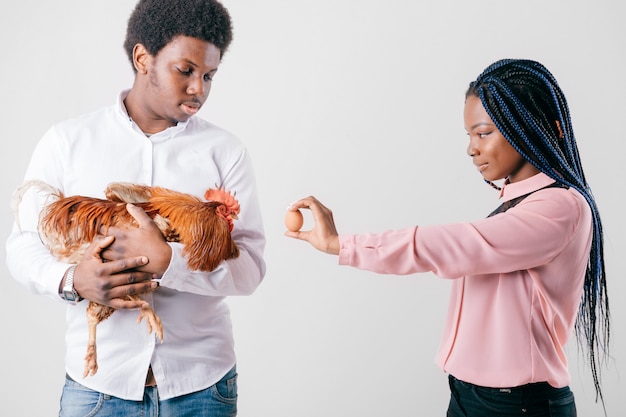 Woman showing egg to chicken hold by man