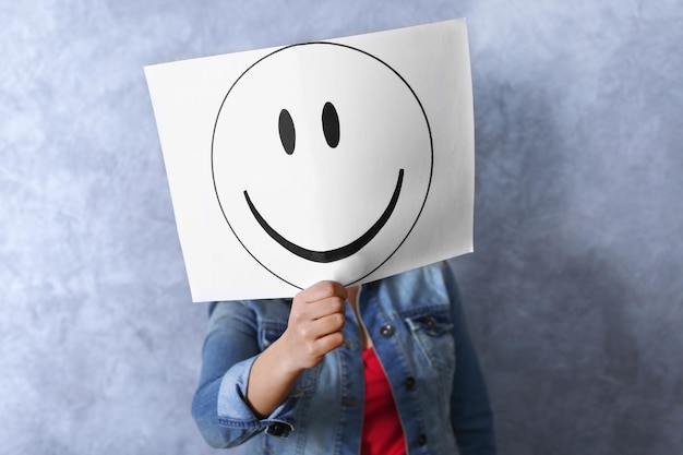 Woman showing a happy emoticon in front of face against a grey textured wall background