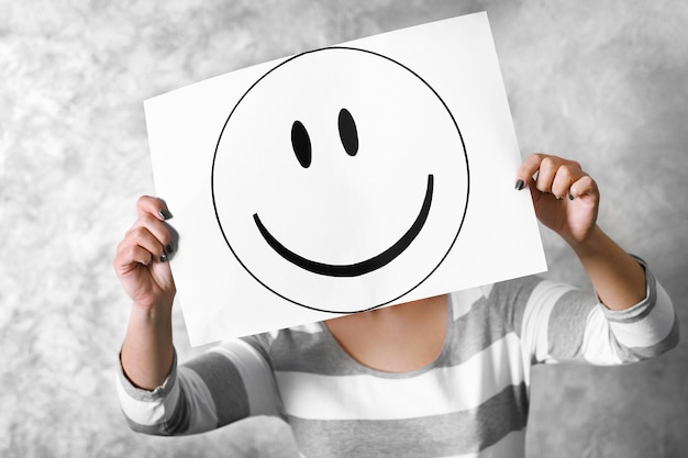 Woman showing a happy emoticon in front of face against a grey textured wall background