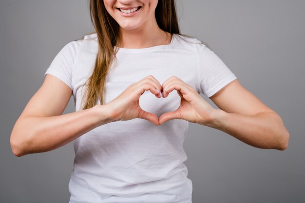 Woman showing heart shape with her hands isolated on grey 