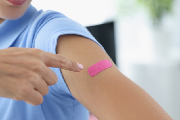 Woman showing her index finger to patch at injection site of flu vaccine closeup. Vaccination against coronavirus infection concept