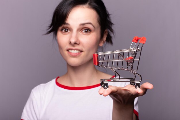 Woman showing mini shopping cart online shop ecommerce concept Grey background