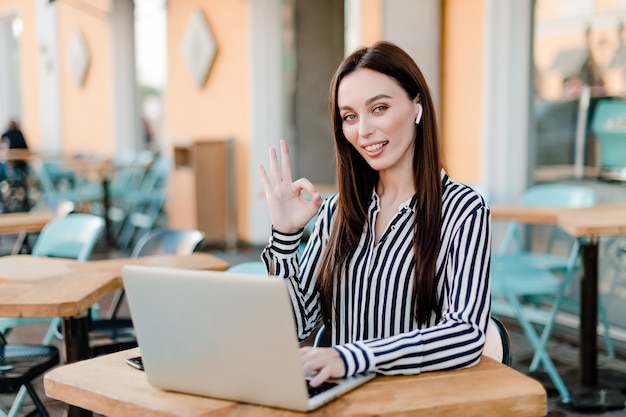 Woman showing ok gesture while working outdoors in the cafe with laptop 