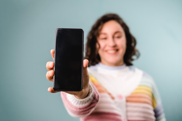 Woman showing a smartphone with a blank screen to camera while standing over an isolated background