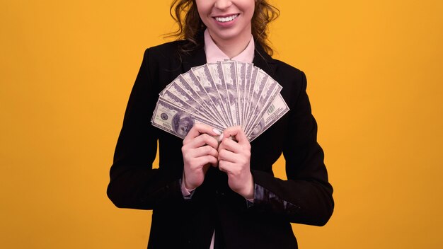 Woman showing a stack of money isolated on yellow.