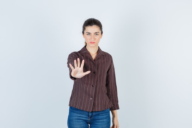 woman showing stop gesture in shirt, jeans and looking resolute. front view.