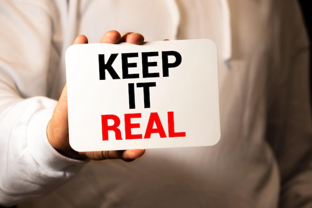 Женщина показывает белую карточку со словом " KEEP IT REAL " Бизнес-концепция