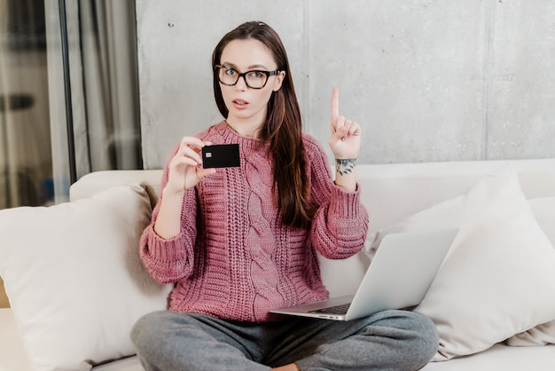 Woman shows credit card from bank at home on a couch