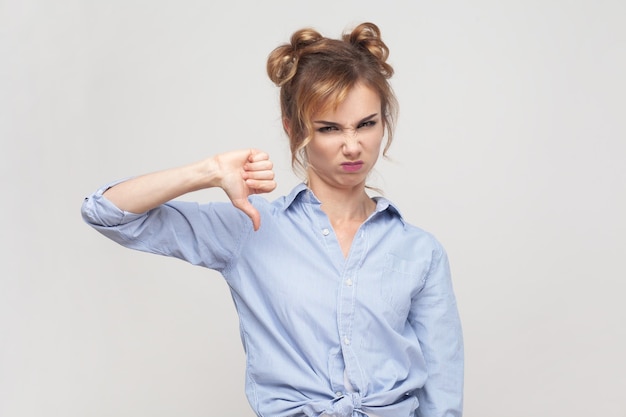 Woman shows disapproval sign keeps thumb down expresses dislike frowning face in discontent