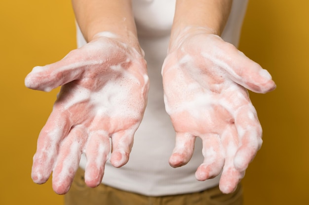 Woman shows her hands in soapy suds on a yellow background