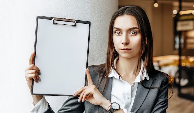 The woman shows information on the tablet. Place for advertising. Business concept. The girl holds the documents and explains the information. White blank sheet of paper.