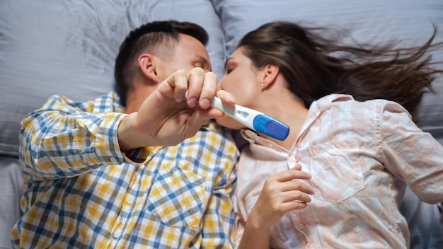 Woman shows a man a pregnancy test lying in bed, top view, happiness