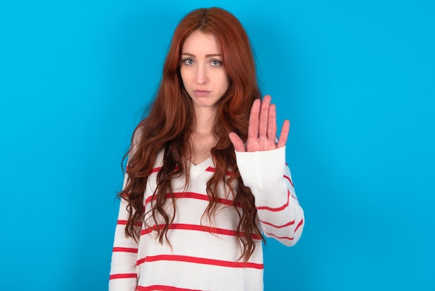 woman shows stop sign prohibition symbol keeps palm forward to camera with strict expression