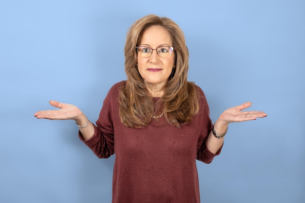 Woman shrugging shoulders with open hands up blue studio background