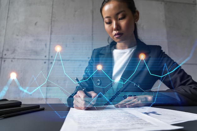 A woman signs contract and financial chart hologram Concept of stock market analysis Multiexposure International business