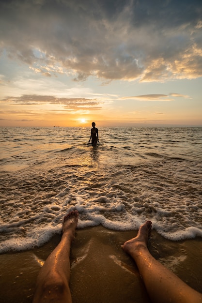 Woman silhouette on the beach at sunset with man legs.