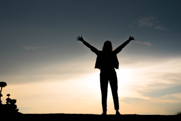 Woman silhouette standing raise hand on sunset