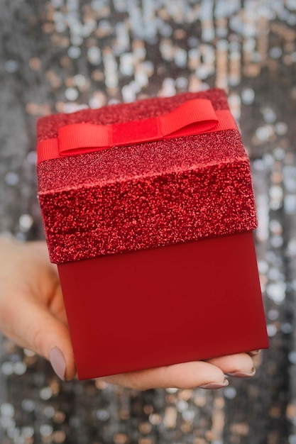 Женщина в серебряном платье держит красную подарочную коробку