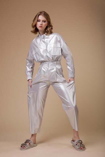 Woman in silver platinum metallic suit jacket pants posing on beige coffee background