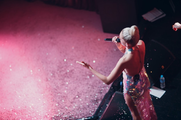 Woman singer with microphone on the stage with sparkles on foreground