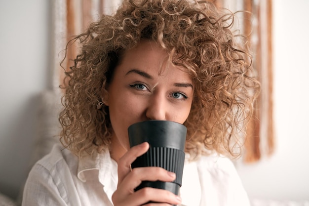 写真 熱い飲み物を飲みながらカメラを見ている女性