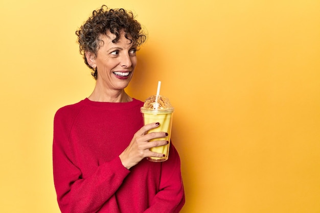 Женщина пьет ванильный коктейль на ярко-желтом фоне студии