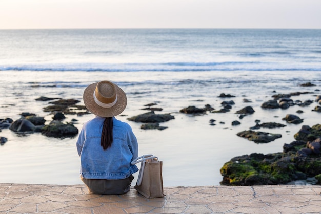 Foto donna seduta accanto alla spiaggia al tramonto