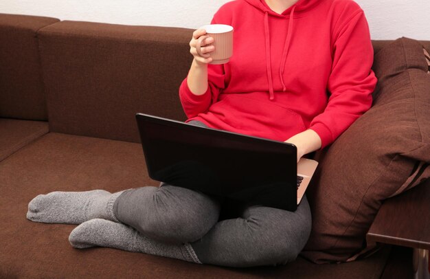 Woman sit on cozy sofa writing email on laptop and drinking\
coffee, girl freelancer working at computer from home, focused\
student studying un bed.