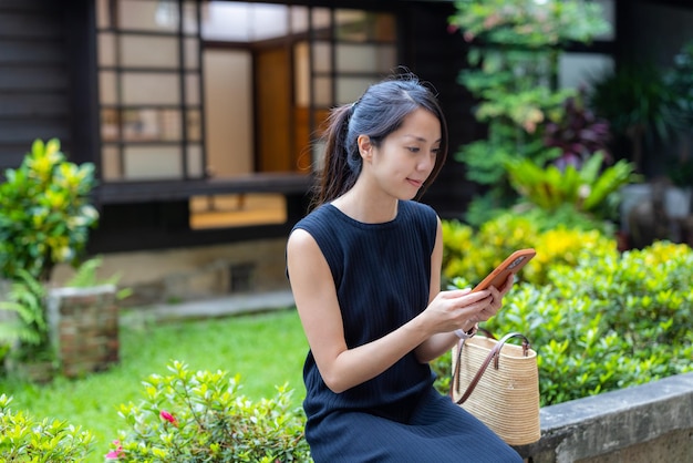 여자 는 일본 정원 에 앉아 휴대 전화 를 사용 한다