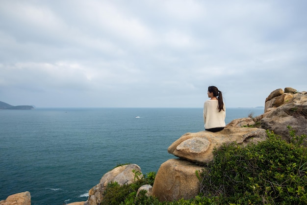 Foto la donna si siede sulla roccia per guardare il mare sulla montagna