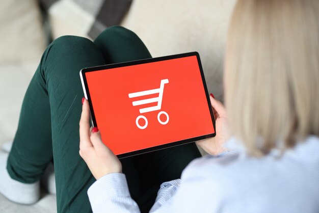 Woman siting on couch and holding tablet in her hands. Online shopping concept