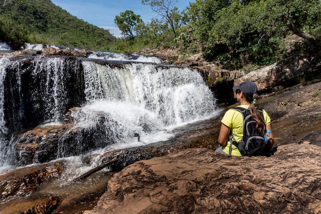 Woman siting on a rock looking at a waterfall ecotourism concept