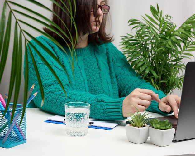 Фото Женщина сидит за белым столом и общается в интернете через ноутбук видео звонок блогирование рабочее место