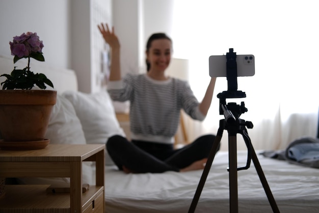a woman sits on a bed and holds up a camera with her hand to her face