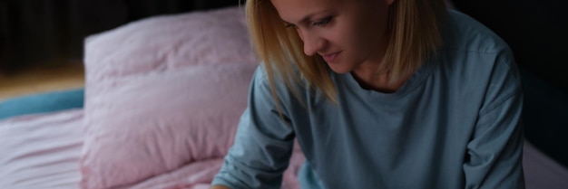 Woman sits on bed and looks into smartphone closeup