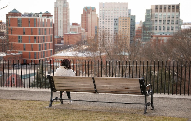 A woman sits on a bench in front of a cityscape.