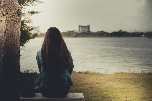 A woman sits on a bench overlooking a lake and the sun is setting.