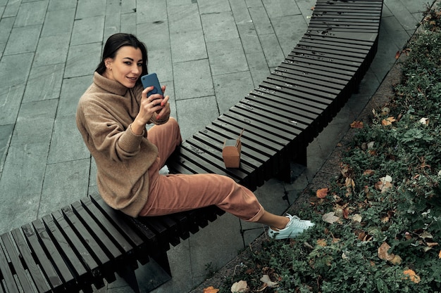 여자는 공원에서 벤치에 앉아 전화 셀카를 걸립니다.