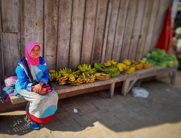 a woman sits on a bench with bananas on it.