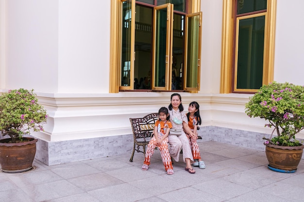 A woman sits on a bench with two children in front of a window that says'the word siam '