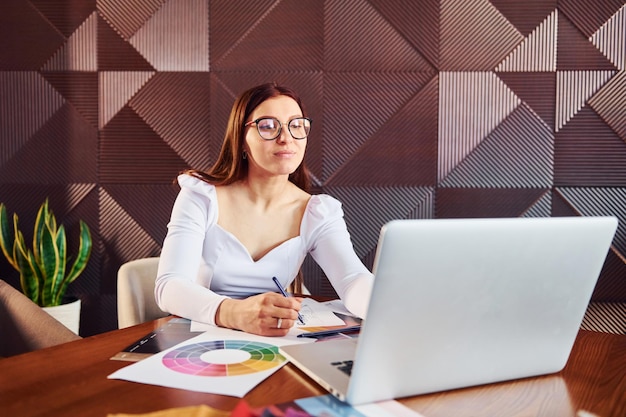 Woman sits by table with laptop and documents indoors of new modern luxury restaurant