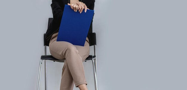 A woman sits in a chair in front of the job interview room\
awaiting the manager\'s interview, holding the supporting documents\
for the job interview. ideas for applying and attending job\
interviews.