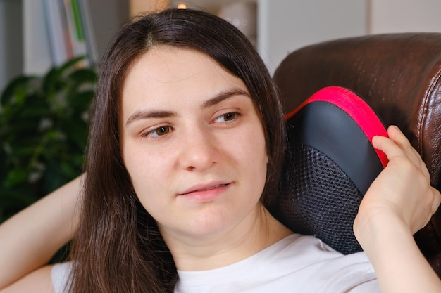 A woman sits in a chair with a massage pillow and does a neck massage
