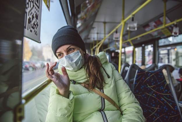 여자는 의료 보호 마스크에 시내 버스에 앉아있다. 대중 교통에서 코로나 바이러스 covid-19에 대한 보호.