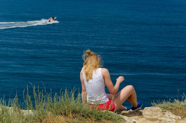 Photo a woman sits on a cliff overlooking the ocean and the ocean.