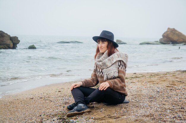 Woman sits on coast against background of rocks against the beautiful sea