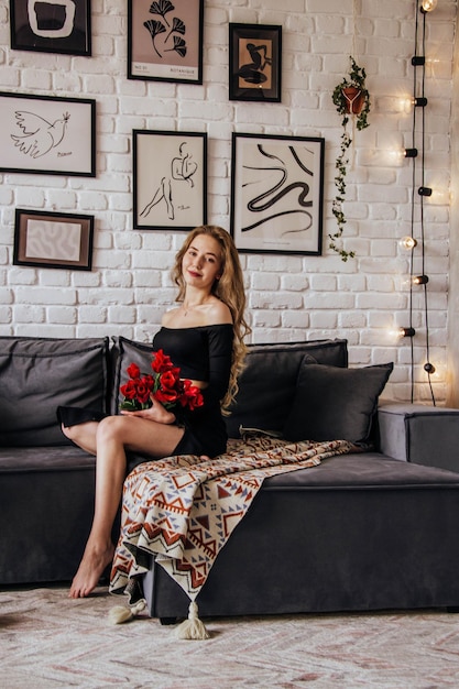 A woman sits on a couch in a room with a white brick wall and a white brick wall with a painting on it.