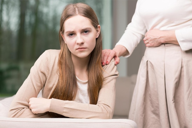 A woman sits on a couch with her hand on her shoulder.