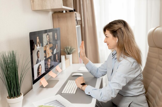 Photo a woman sits at a desk and points to a screen with a photo of a group of people.