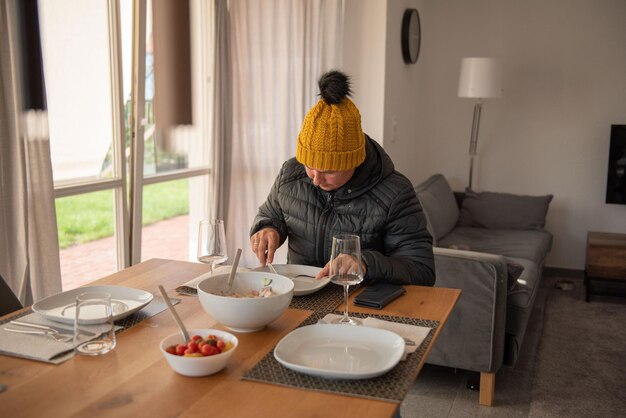 女性が暖かく服を着てダイニングテーブルに座って食べています